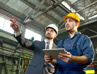 Waist up portrait of handsome businessman pointing up while discussing something with factory worker holding digital tablet, copy space