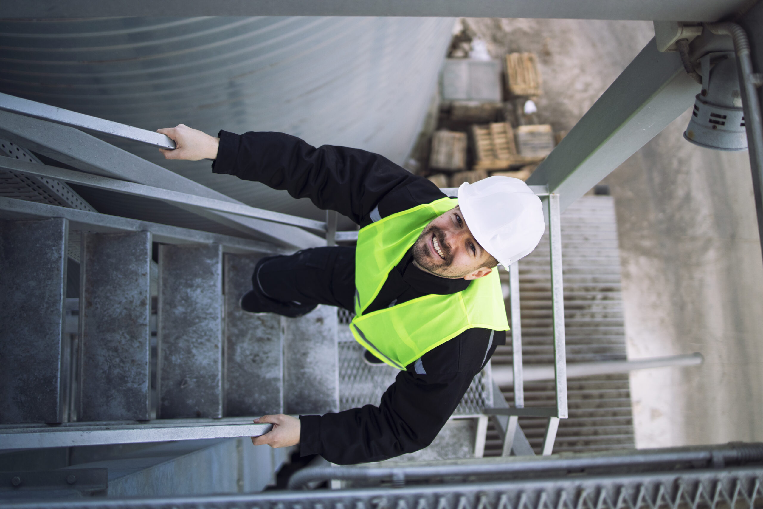 Top view of factory worker climbing metal stairs on industrial silo building.